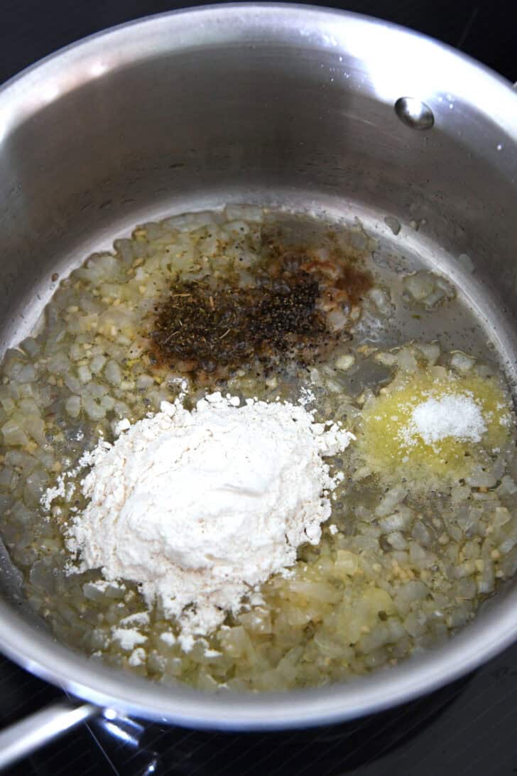 Top down view of a metal pot with sautéed onions, spices, and flour.