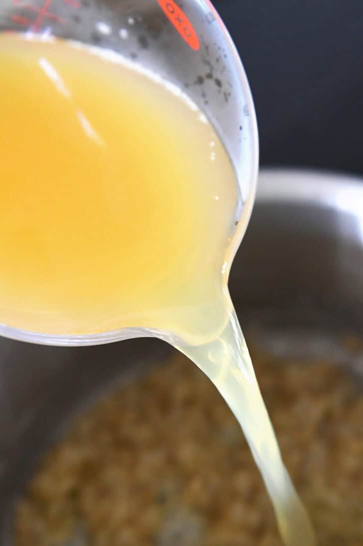 A measuring cup pouring chicken broth into a stock pot.
