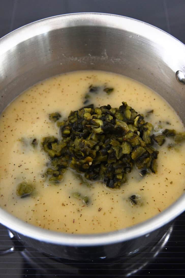 A metal pot filled with a broth mixture and roasted, diced green peppers piled on top.