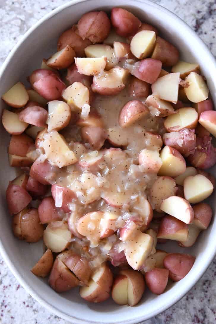 Top down view of a white oval dish with large potato chunks and an onion sauce spread over the top.