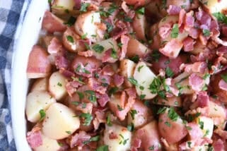 Top down view of a white oval dish with potato chunks, bacon pieces, and chopped parsley.