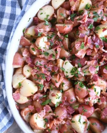 Top down view of a white oval dish with potato chunks, bacon pieces, and chopped parsley.
