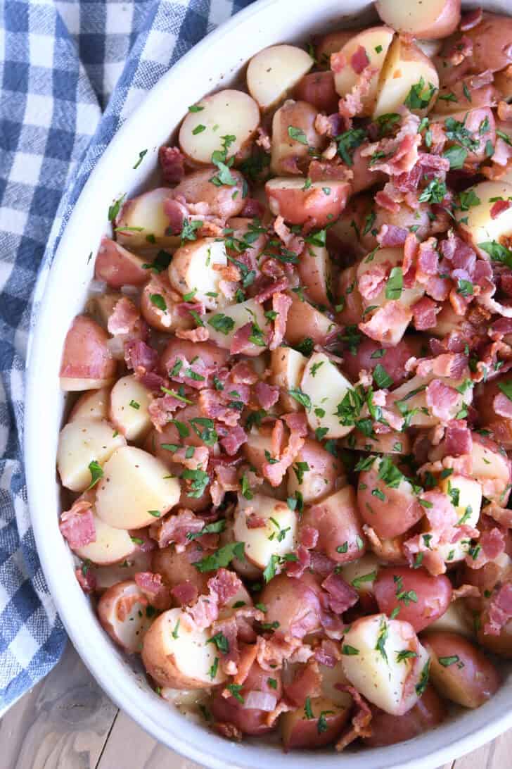 Top down view of a white oval dish with potato chunks, bacon pieces, and chopped parsley.