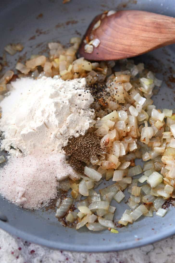 Top down view of a skillet with spices, sautéed onions, and flour.