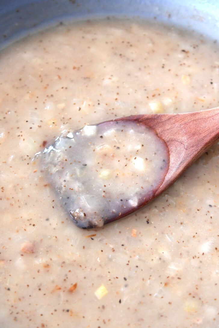 A wooden spoon in a skillet full of a white onion sauce.