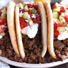 Front view of three stuffed greek flatbread tacos topped with tzatziki sauce, chopped cucumbers, and diced tomatoes.