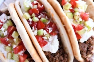 Top down view of three loaded greek flatbread tacos loaded with tzatziki sauce, diced cucumbers, and chopped tomatoes.