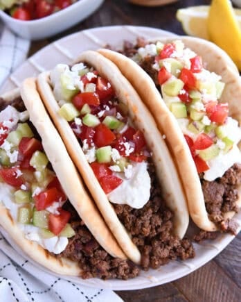 Top down view of three loaded greek flatbread tacos loaded with tzatziki sauce, diced cucumbers, and chopped tomatoes.