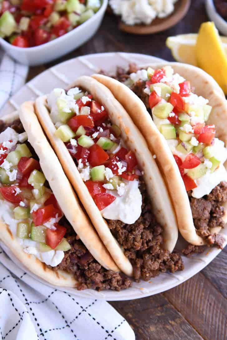 Top down view of three loaded greek flatbread tacos loaded with tzatziki sauce, diced cucumbers, and chopped tomatoes.