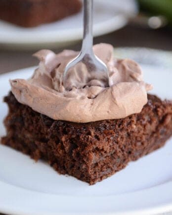 Chocolate zucchini cake with chocolate frosting on white plate.