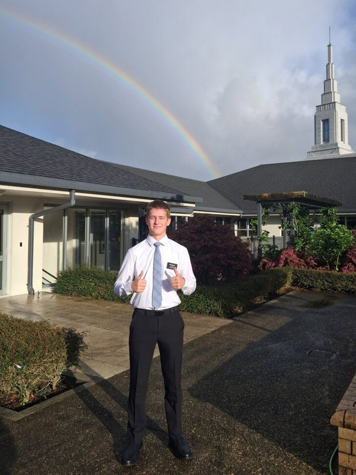 Young man in shirt and tie standing in front of building with rainbow.