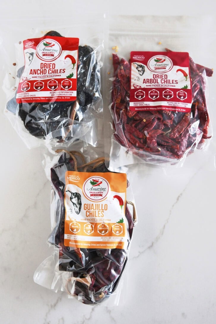 Dried ancho chiles, dried arbo chiles, and dried guajillo chiles in plastic cellophane bags.