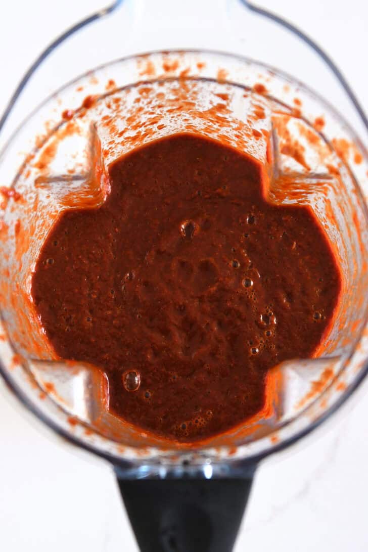 Top down view of blender with blended mixture of Mexican chiles, onion, and broth.