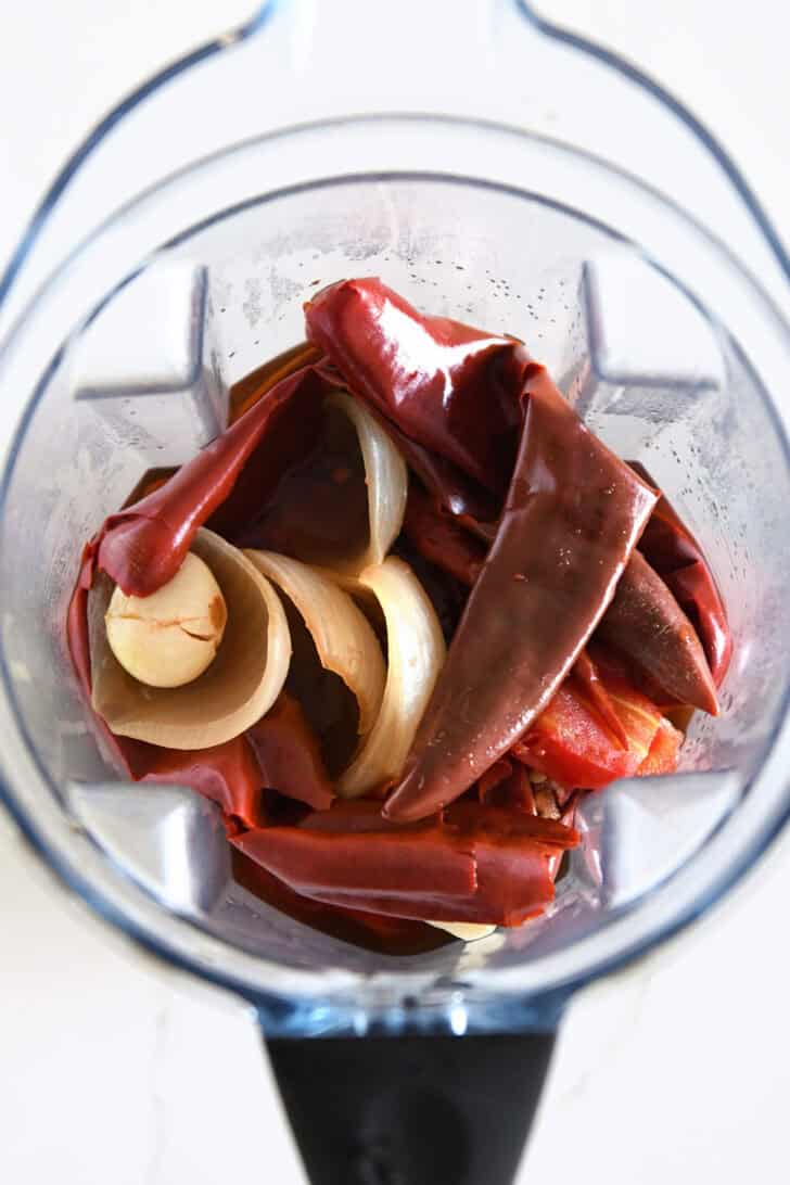 Top down view of blender with soft boiled Mexican chiles, cooked onions, and garlic.