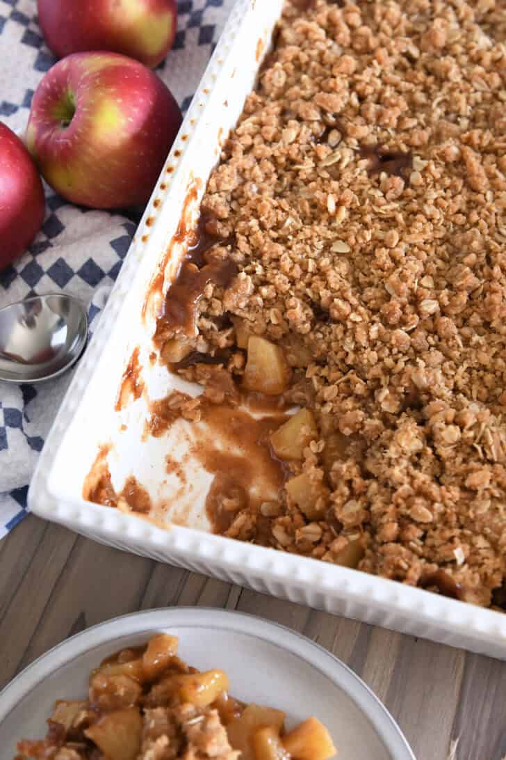Top down view of caramel apple crisp in white 9X13-inch pan with one serving removed from the corner.