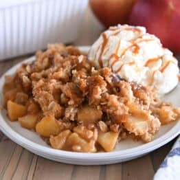 Serving of caramel apple crisp on gray plate with ice cream also drizzled with caramel.