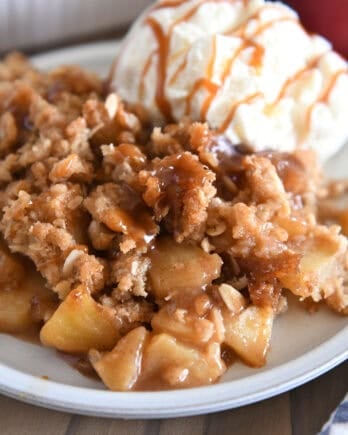 Serving of caramel apple crisp on gray plate with scoop of ice cream.