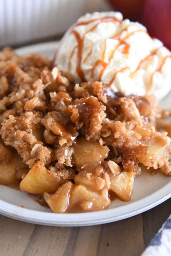 Serving of caramel apple crisp on gray plate with scoop of ice cream.
