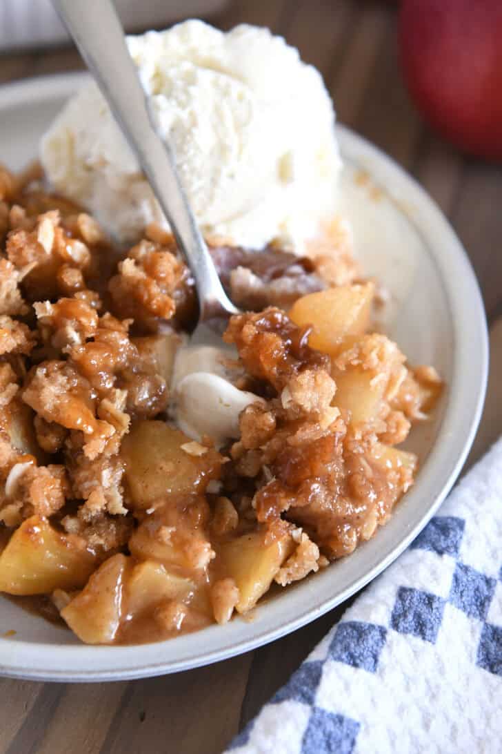 Serving of caramel apple crisp on gray plate with scoop of ice cream.