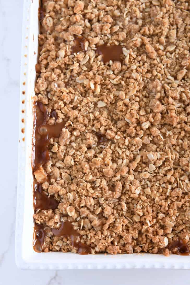 Top down view of bottom left corner of white 9X13-inch pan of caramel apple crisp.