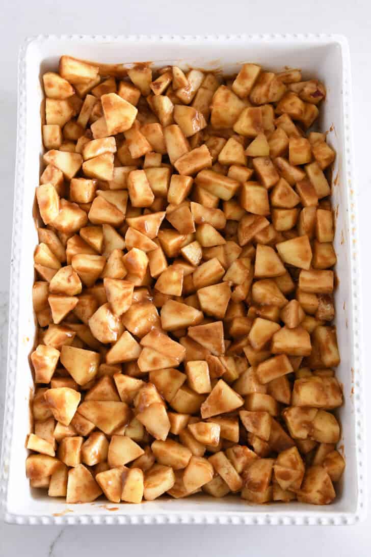 Top down view of chopped apples mixed with caramel sauce in white 9X13-inch baking dish.