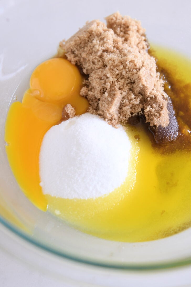 Glass bowl with eggs, brown sugar, olive oil and granulated sugar.