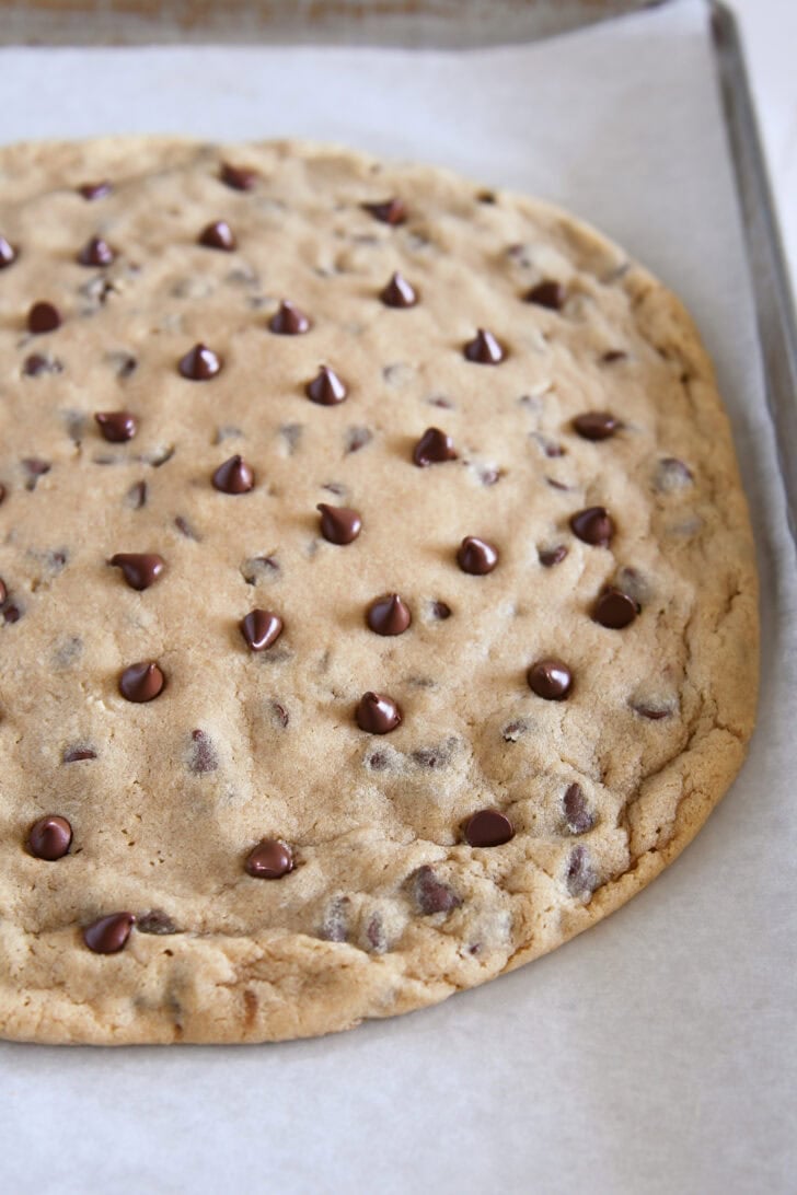 A large chocolate chip cookie on a piece of parchment paper.