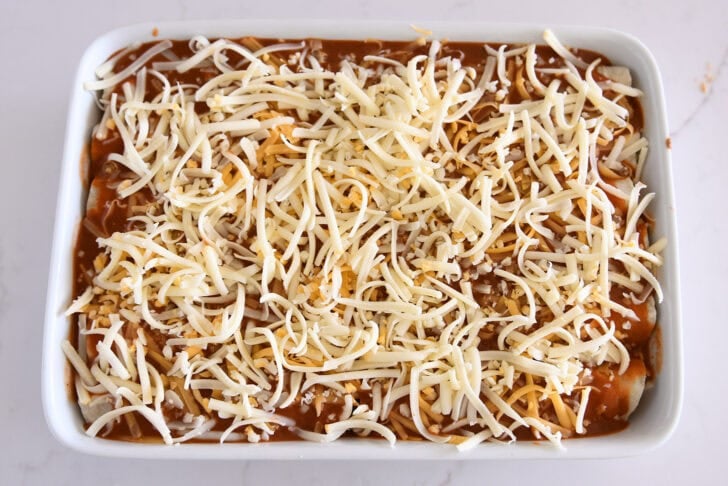 Top down view of white 9X13-inch pan filled with ground beef enchiladas and topped with enchilada sauce and shredded cheese.