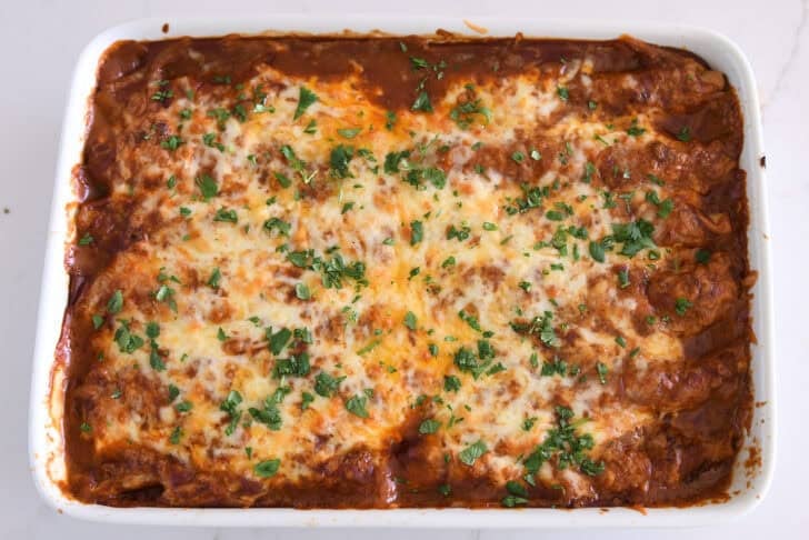 Top down view of baked pan of ground beef enchiladas with red sauce, melted cheese and cilantro.