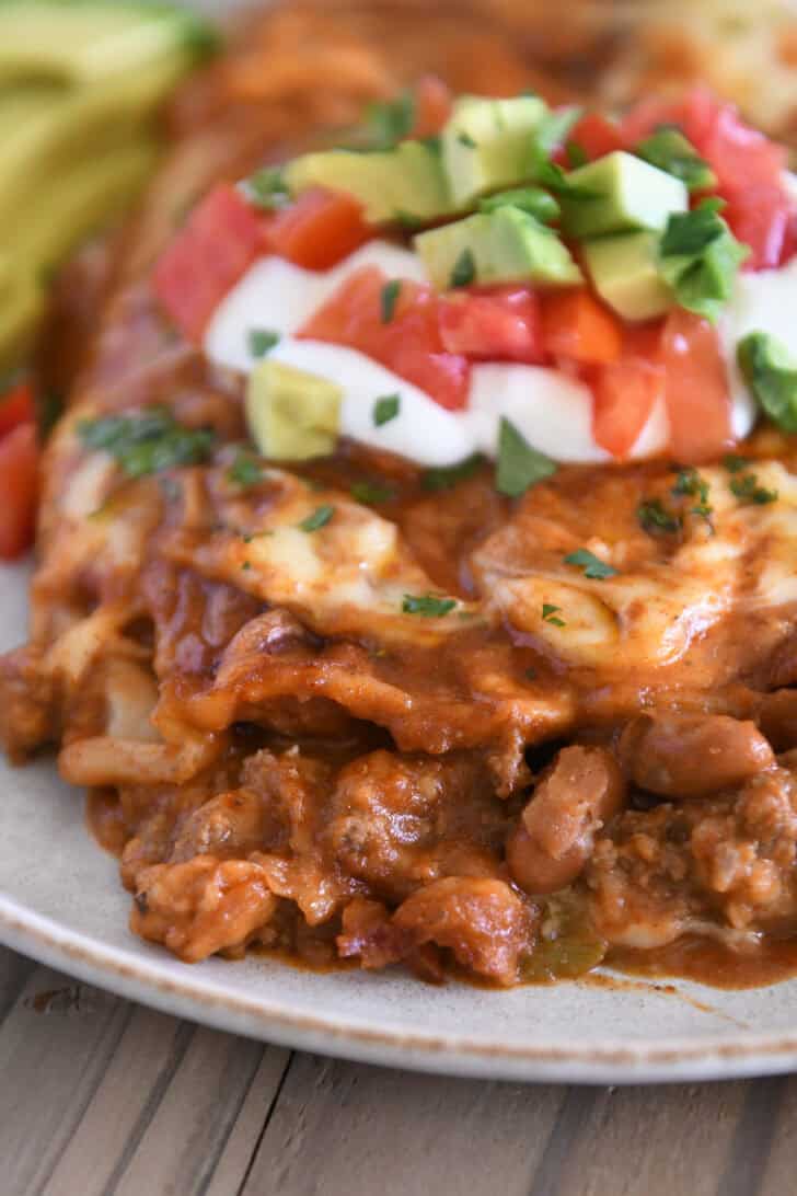 Close up view of a red sauce ground beef enchilada on gray plate; the filling is ground beef and pinto beans.
