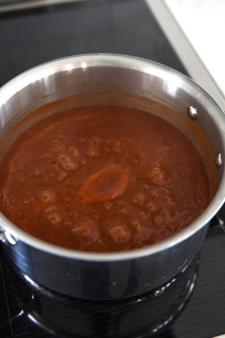 Homemade from-scratch red enchilada sauce simmering in stainless saucepan on induction stove.