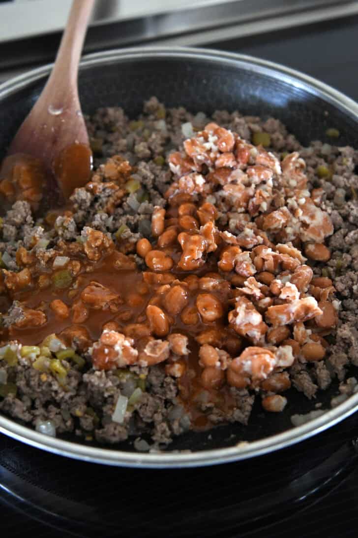 A 12-inch nonstick skillet with cooked ground beef, green chiles, mashed pinto beans and enchilada sauce.