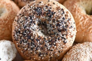 Lots of homemade bagels together on baking sheet with the center bagel loaded with everything bagel seasoning.