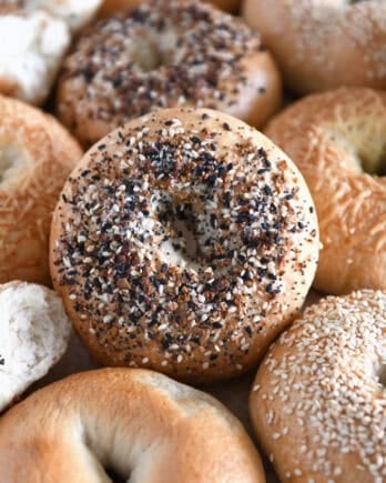 Lots of homemade bagels together on baking sheet with the center bagel loaded with everything bagel seasoning.