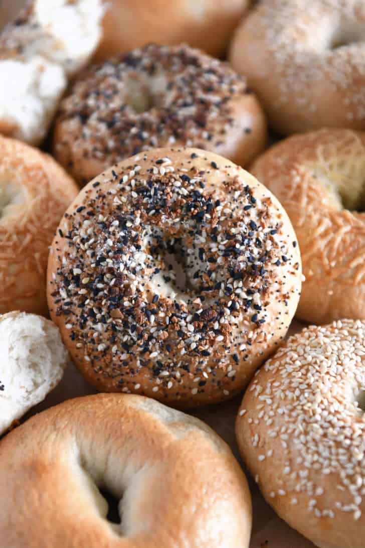 Lots of homemade bagels together on baking sheet with the center bagel loaded with everything bagel seasoning.