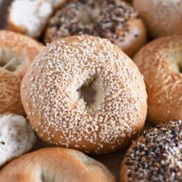 Lots of homemade bagels together on baking sheet with the center bagel loaded with sesame seeds.