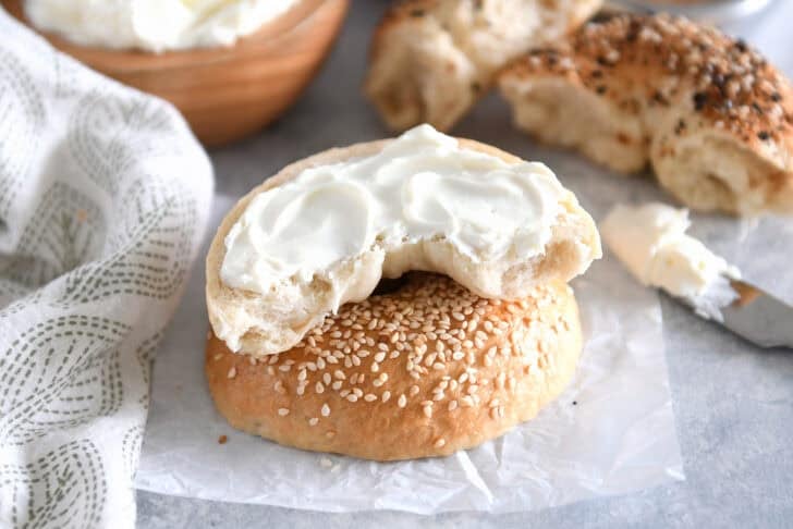 One half of homemade bagel slathered with cream cheese on top of sesame seed top half.