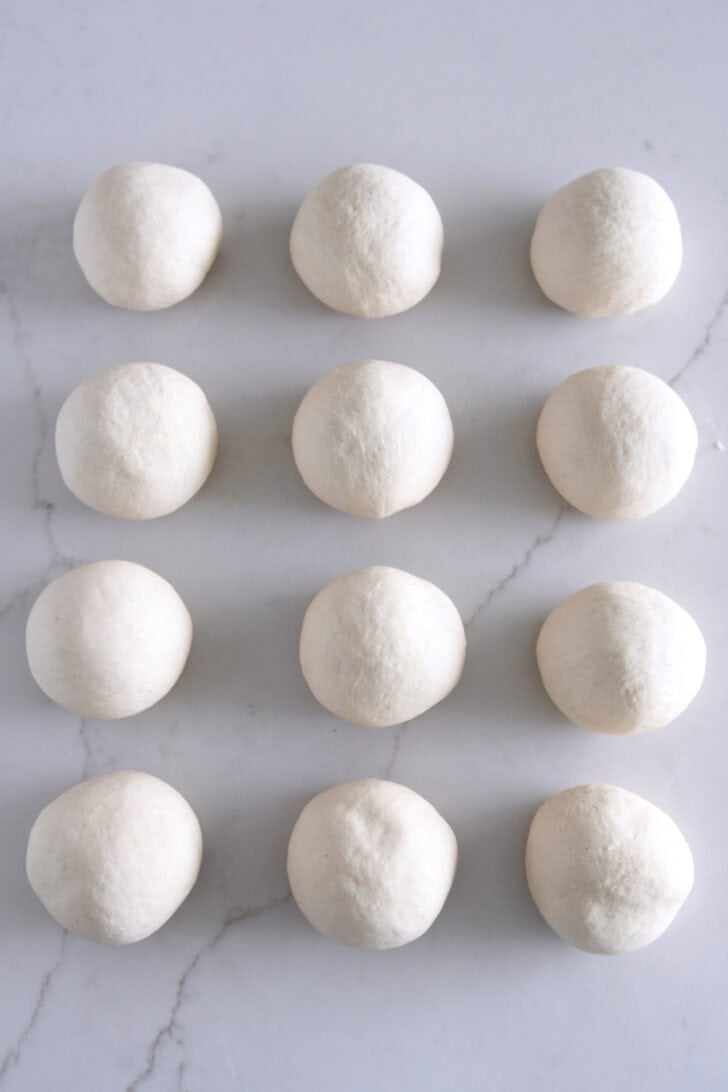 12 round dough balls on white counter.