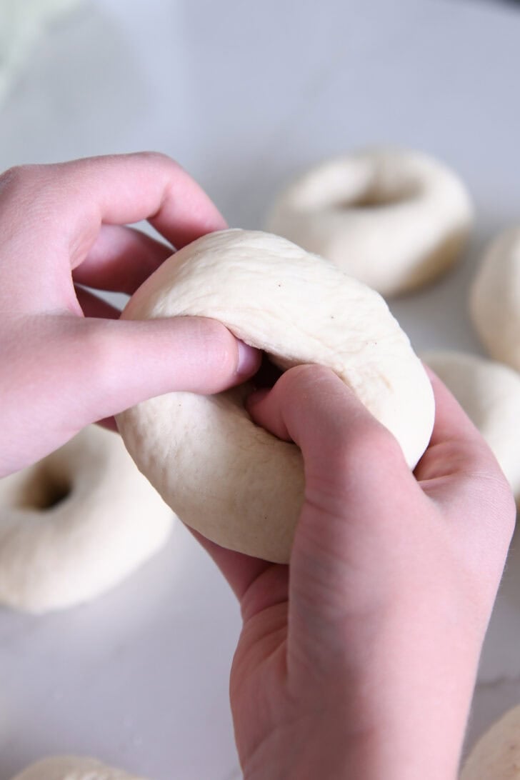 Pressing thumbs into dough ball to form bagel.
