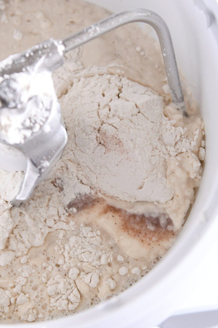 White Bosch bowl fitted with the dough hook with flour, sourdough starter, water and salt.