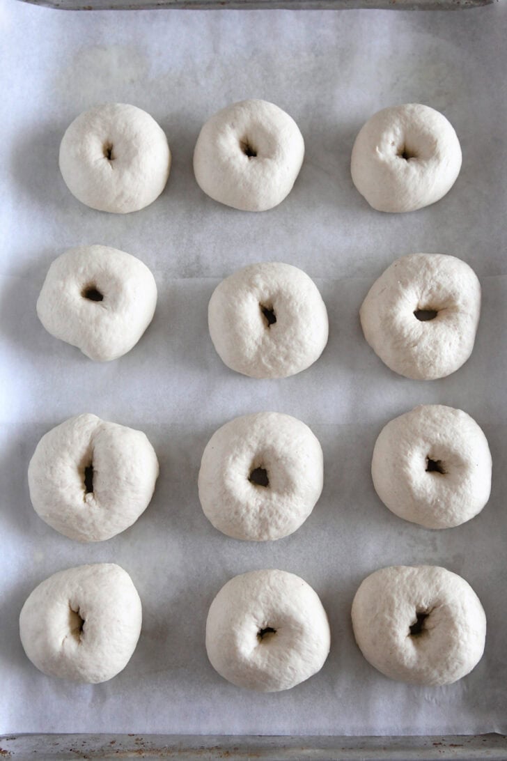 Top down view of 12 shaped bagels on half sheet pan.