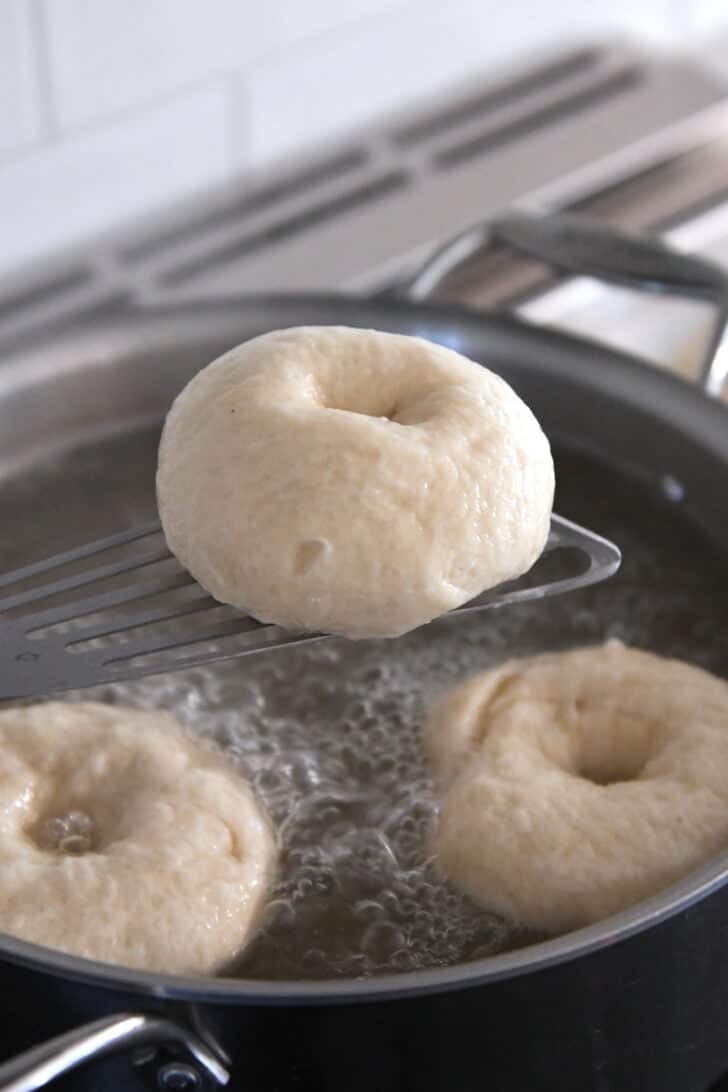 Lifting bagel out of boiling water bath with spatula.