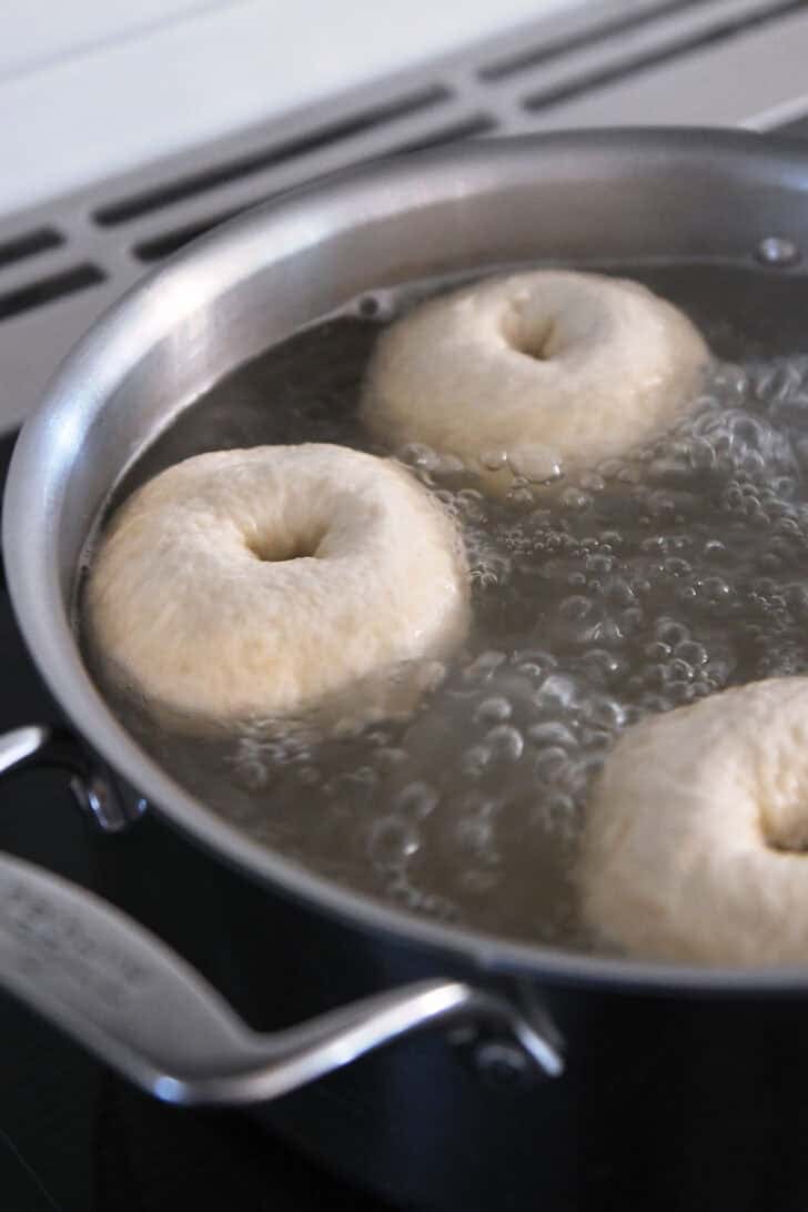 Three bagels boiling in water bath.