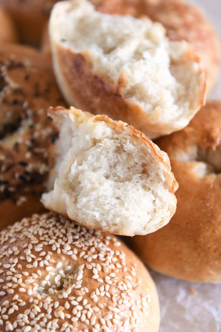 Bagel torn in half on top of other baked bagels.