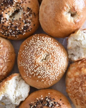 Top down view of sesame seed topped bagel with several other baked bagels.