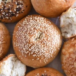 Top down view of sesame seed topped bagel with several other baked bagels.