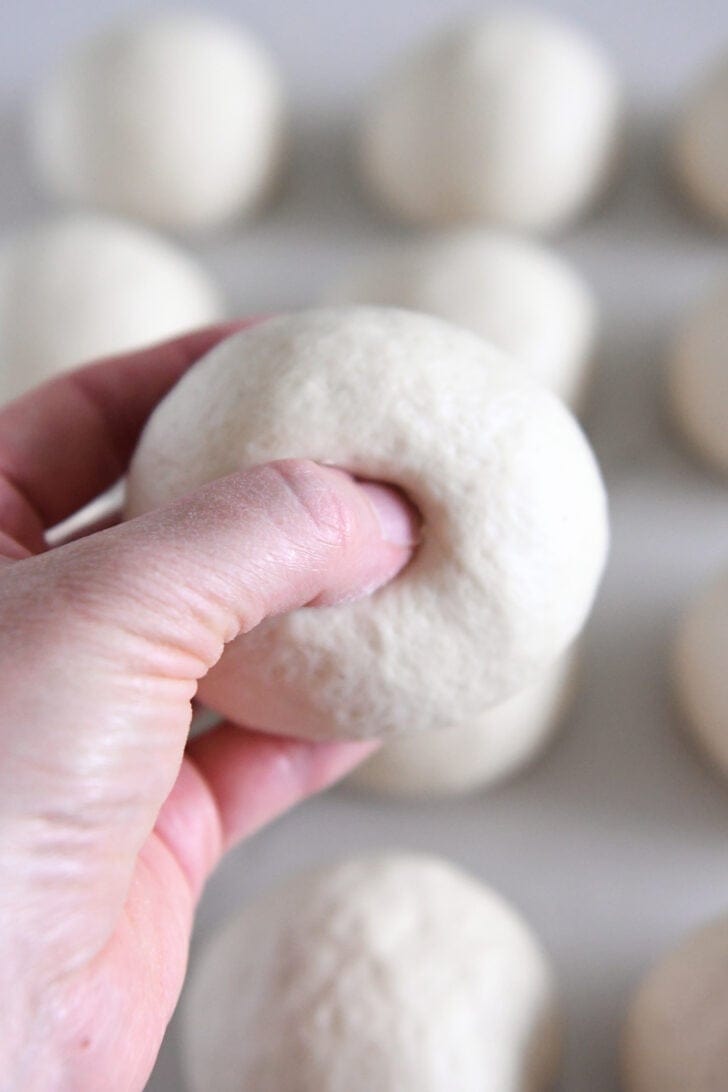 Pressing thumb through center of ball of sourdough bagel dough.