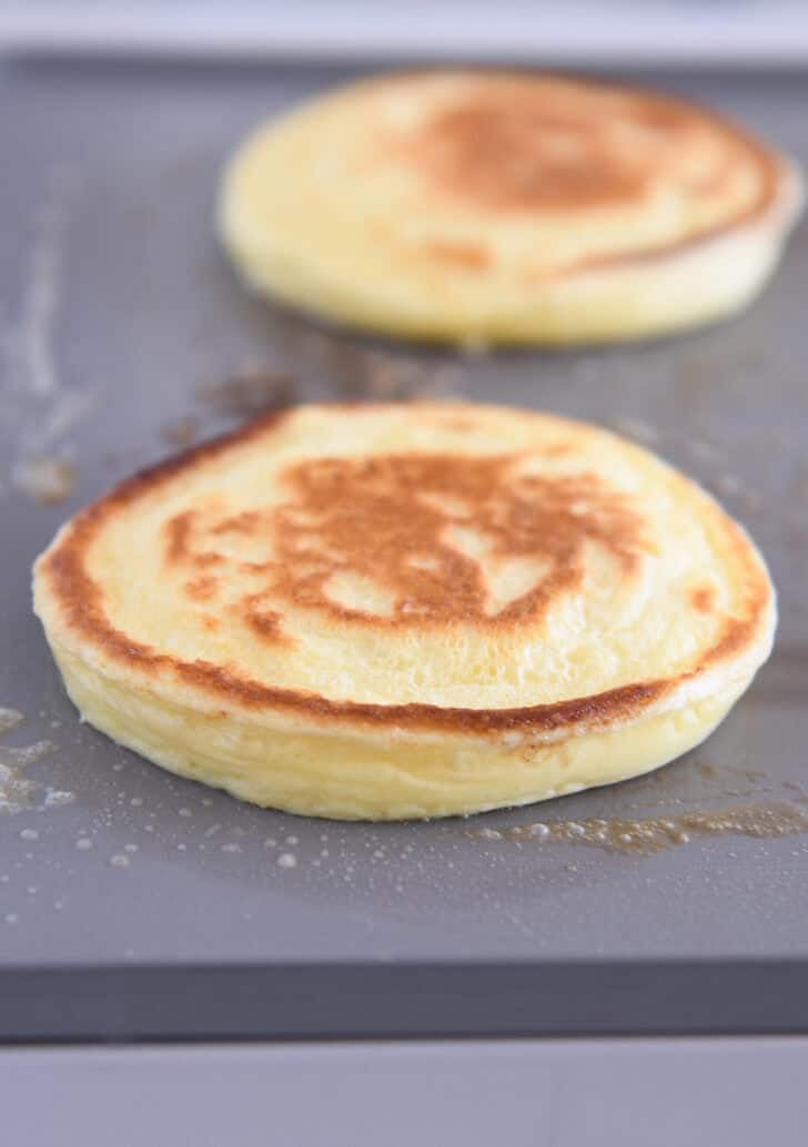 Fluffy cottage cheese pancake cooking on buttered griddle.