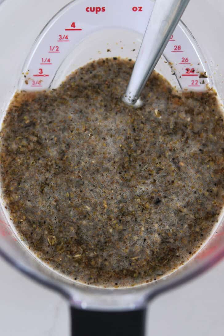 Liquid measuring cup with beef broth, dried oregano, dried basil and dried thyme seasonings.