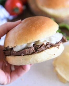 Slow cooker beef on crusty rolls with provolone cheese and one bite taken out; hand holding sandwich.